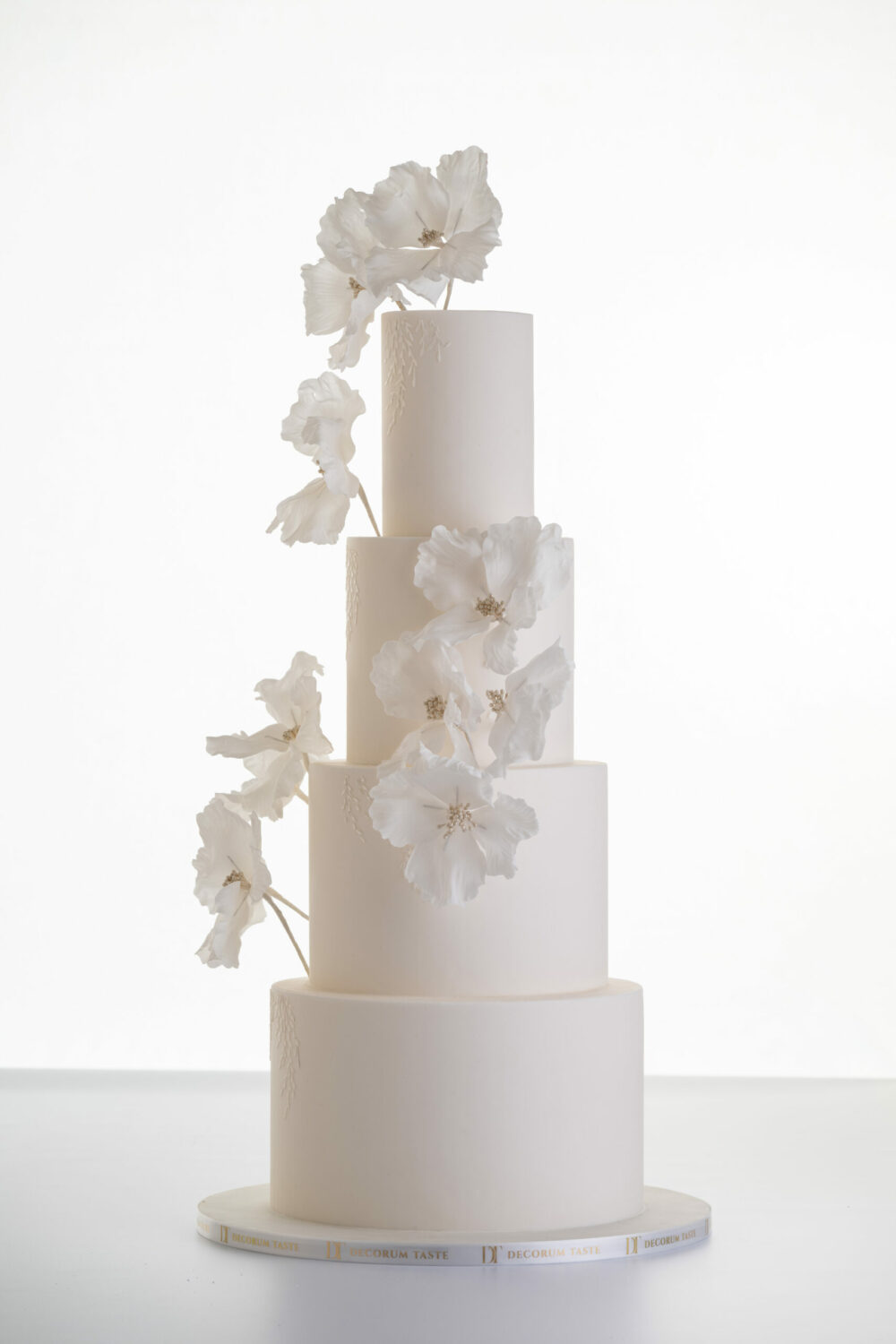 Luxury contemporary 4 tier, customisable wedding cake in ivory with delicate decorative piping and stems of hand-crafted sugar flowers, by Decorum Taste.