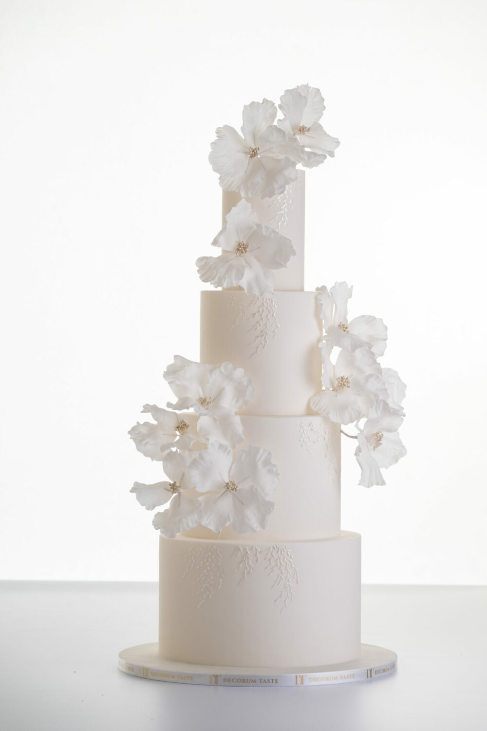 Luxury contemporary 4 tier, customisable wedding cake in ivory with delicate decorative piping and stems of hand-crafted sugar flowers, by Decorum Taste.