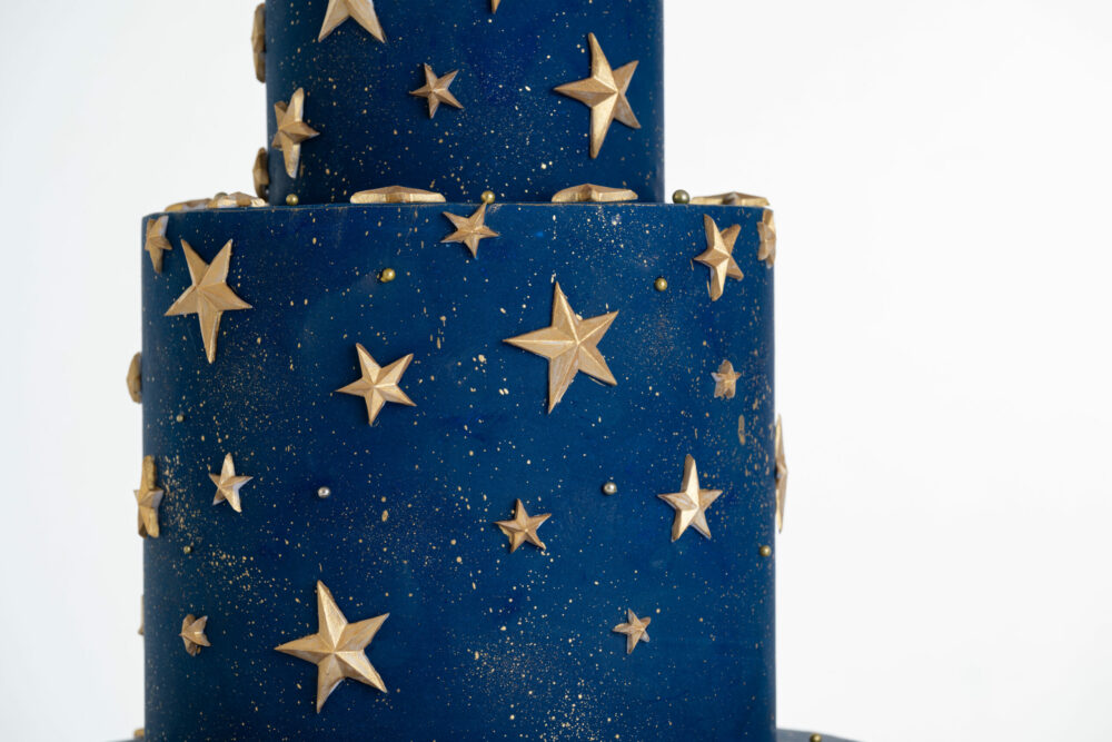 Details of luxury contemporary, customisable, celebration cake, Cosmos Star by Decorum Taste, in deep blue with flecks of edible gold and golden stars.