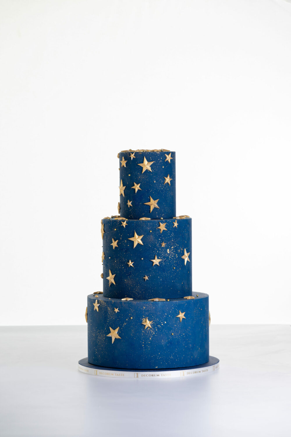 Three tier luxury contemporary, customisable, celebration cake, Cosmos Star by Decorum Taste, in deep blue with flecks of edible gold and golden stars.