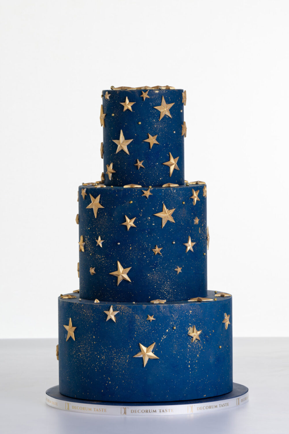 Three tier luxury contemporary, customisable, celebration cake, Cosmos Star by Decorum Taste, in deep blue with flecks of edible gold and golden stars.