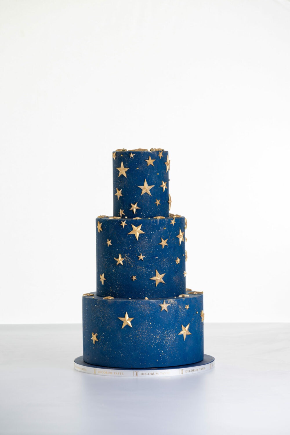 Three tier luxury contemporary, customisable, celebration cake, Cosmos Star by Decorum Taste, in deep blue with flecks of edible gold and golden stars.