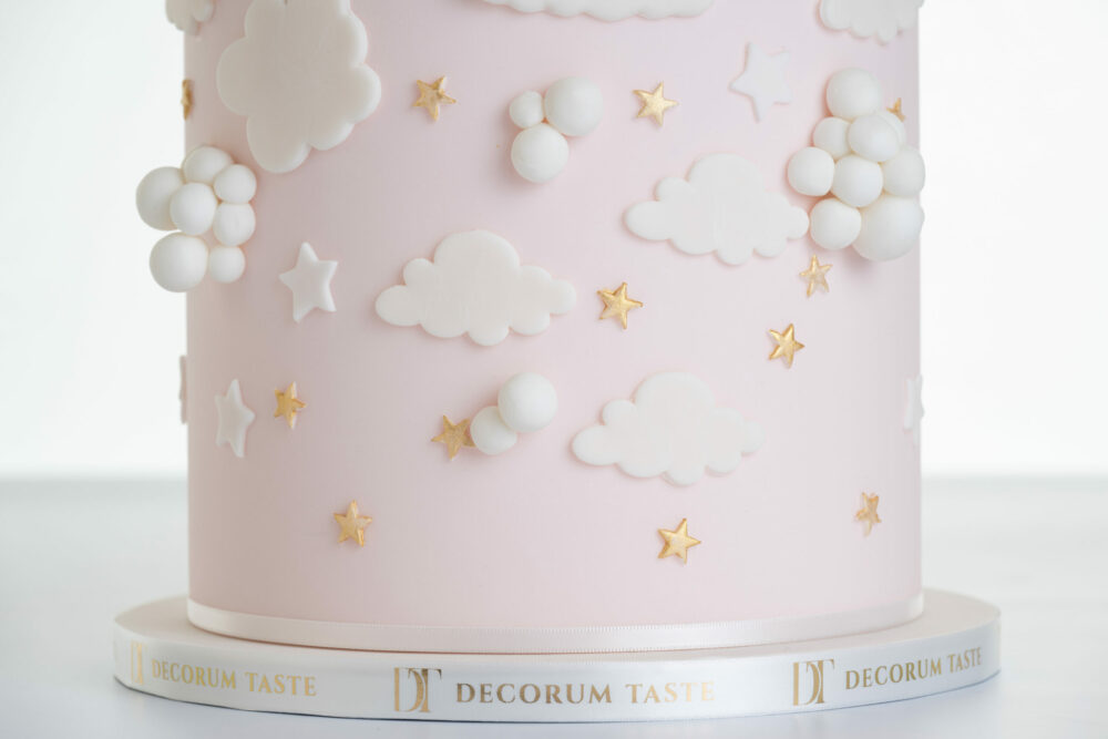 Bottom of luxury contemporary, customisable, celebration cake, Cute Elephant by Decorum Taste, in blush pink with embellishments of clouds, stars and hearts. The side of the cake board is wrapped in a ribbon with the Decorum Taste logo.