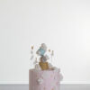 Single tier luxury contemporary, customisable, celebration cake, Cute Elephant by Decorum Taste, in blush pink with hand-crafted elephant in sugar paste sitting on top balancing a balloon, with embellishments of clouds, stars and hearts.