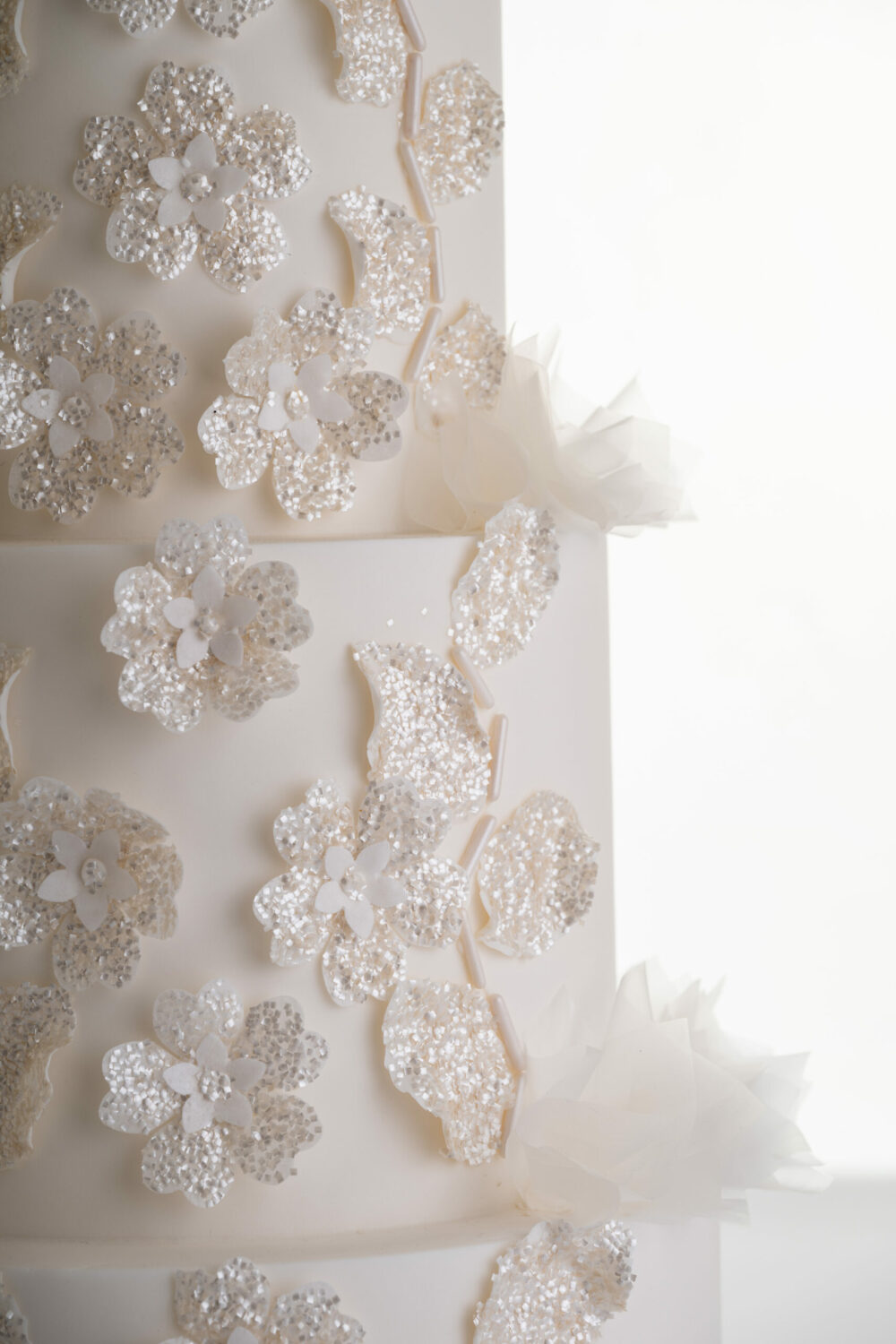 Glittery floral decorative detail and delicate rice paper ruffles on the 4 tier luxury customisable wedding cake, Daphne, by Decorum Taste.