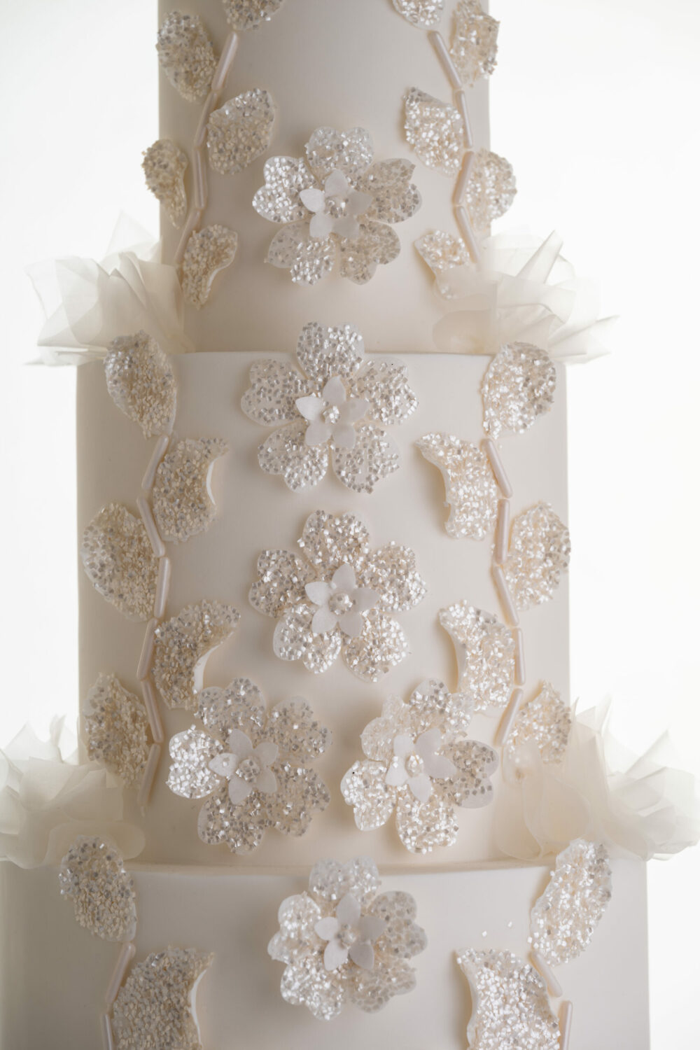 Sequinned floral decorative detail and delicate rice paper ruffles on the 4 tier luxury customisable wedding cake, Daphne, by Decorum Taste.