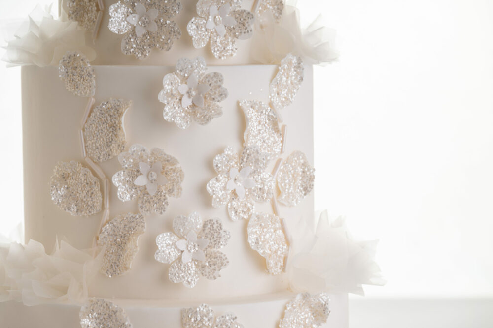 Glittery floral decorative detail and delicate rice paper ruffles on the 4 tier luxury customisable wedding cake, Daphne, by Decorum Taste.