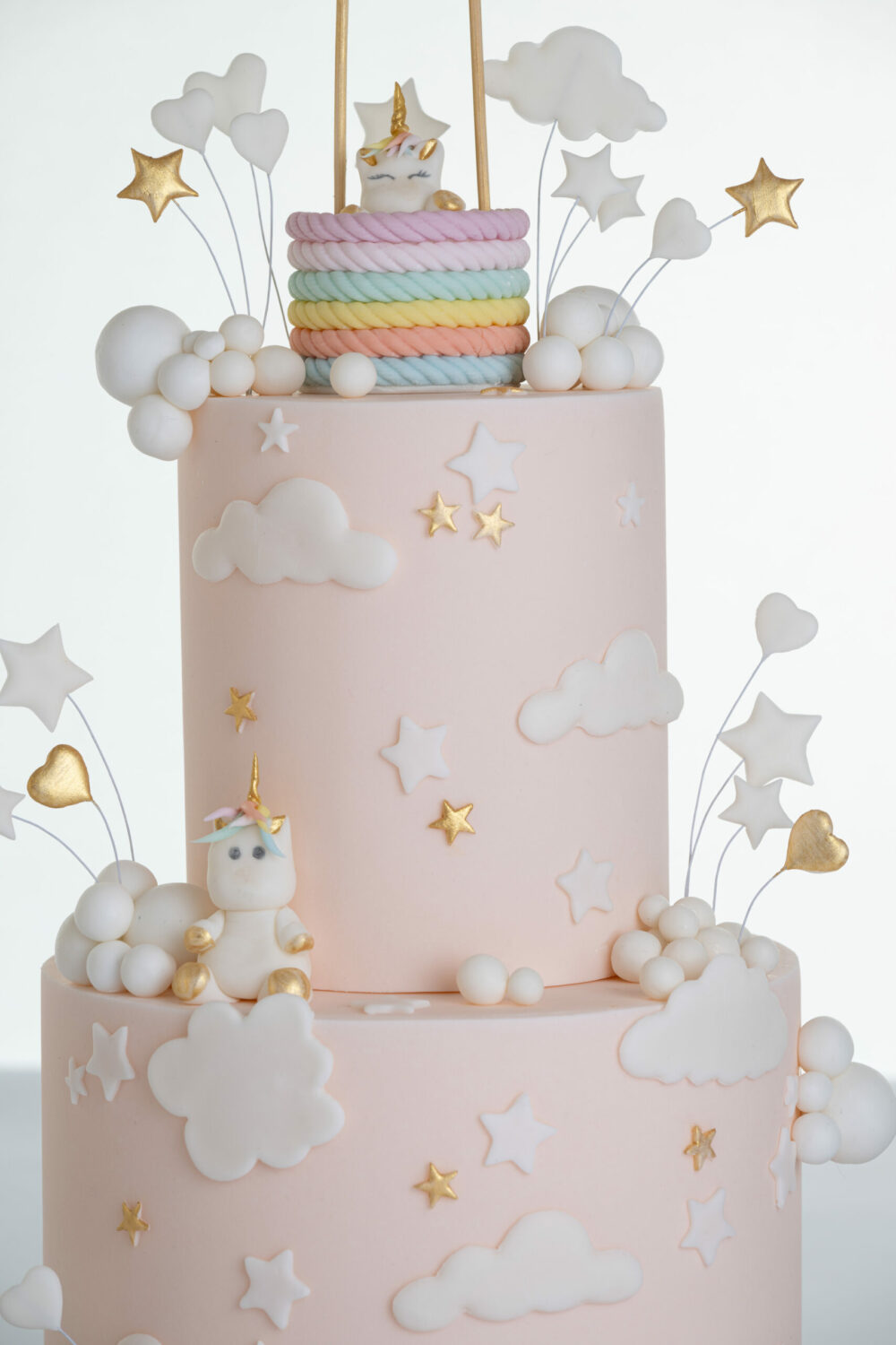 Detail of luxury contemporary, customisable celebration cake, Floating Unicorn by Decorum Taste, decorated in blush pink with embellishments of white clouds, stars with a unicorn at the top sitting in a pastel coloured hot air balloon and another resting on the top of the first tier.