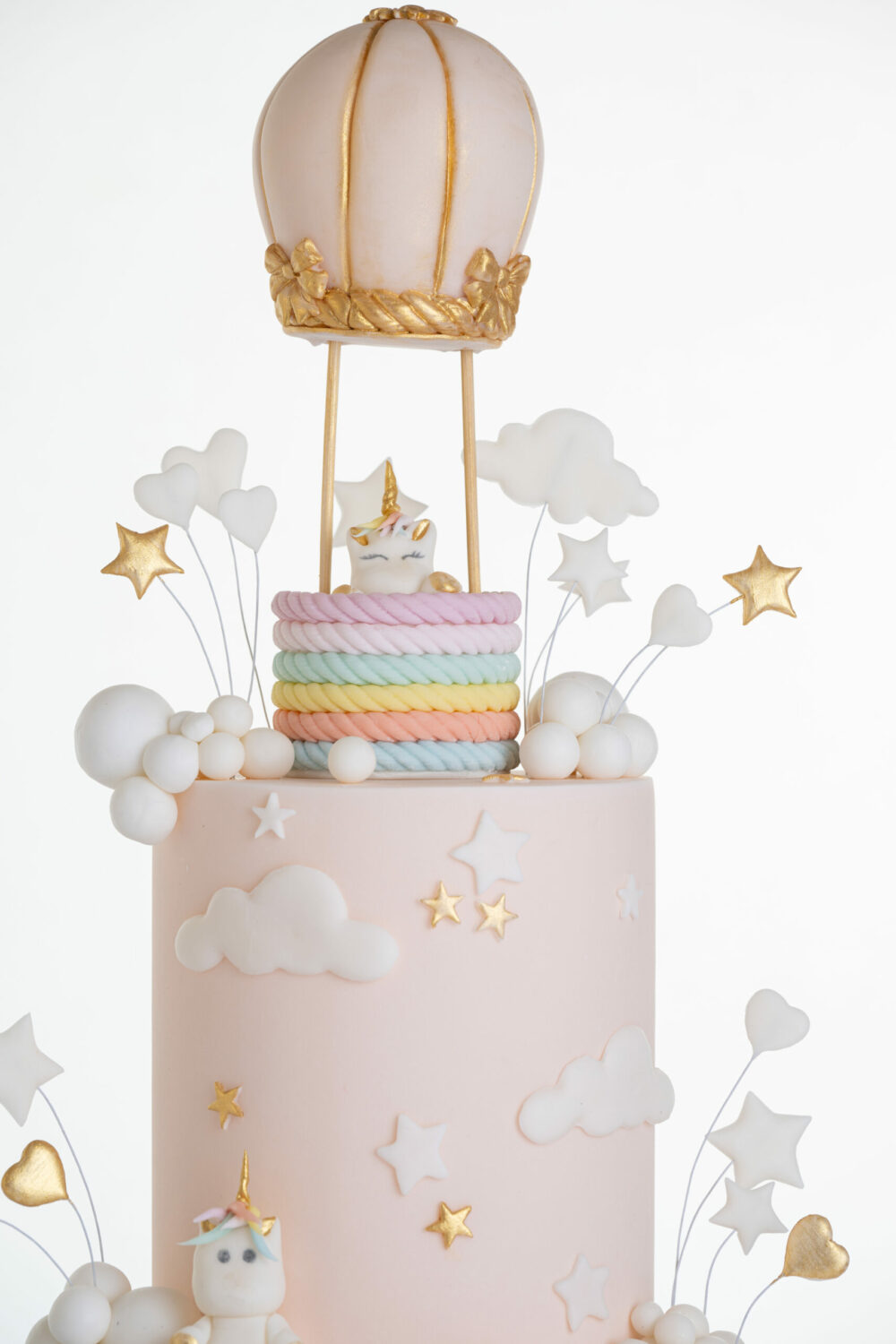 Top tier of luxury contemporary, customisable celebration cake, Floating Unicorn by Decorum Taste, decorated in blush pink with embellishments of white clouds, stars and a unicorn at the top sitting in a pastel coloured hot air balloon.