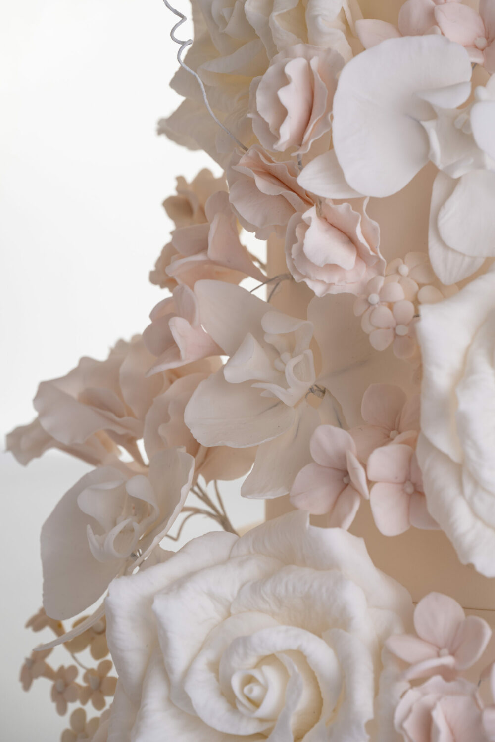 Details of luxury contemporary, customisable, wedding cake, Floral Cascade by Decorum Taste, decorated with hand-crafted sugar roses, sweet peas and other petals in ivory and blush pink tones.