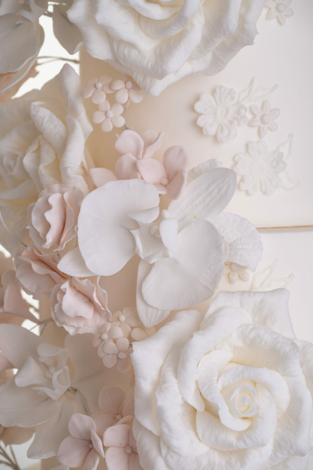 Details of luxury contemporary, customisable, wedding cake, Floral Cascade by Decorum Taste, decorated with hand-crafted sugar roses, sweet peas and other petals in ivory and blush pink tones.