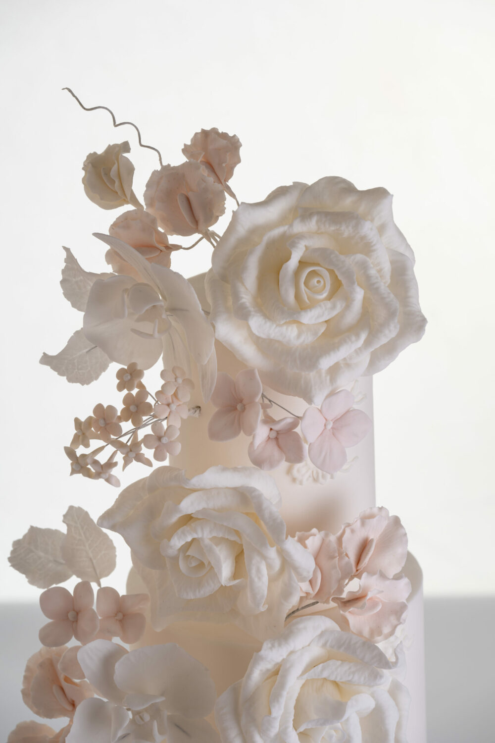 Top two tiers of luxury contemporary, customisable, wedding cake, Floral Cascade by Decorum Taste, decorated with hand-crafted sugar roses, sweet peas and other petals in ivory and blush pink tones.