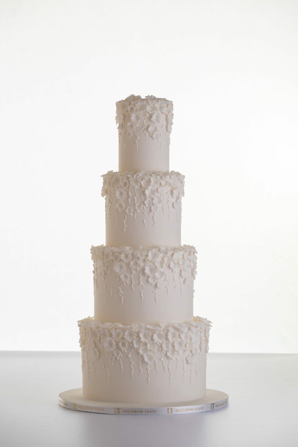 Four tier luxury contemporary, customisable, wedding cake, Fountain of Blossom, by Decorum Taste with cascades of decorative floral embellishments in ivory.