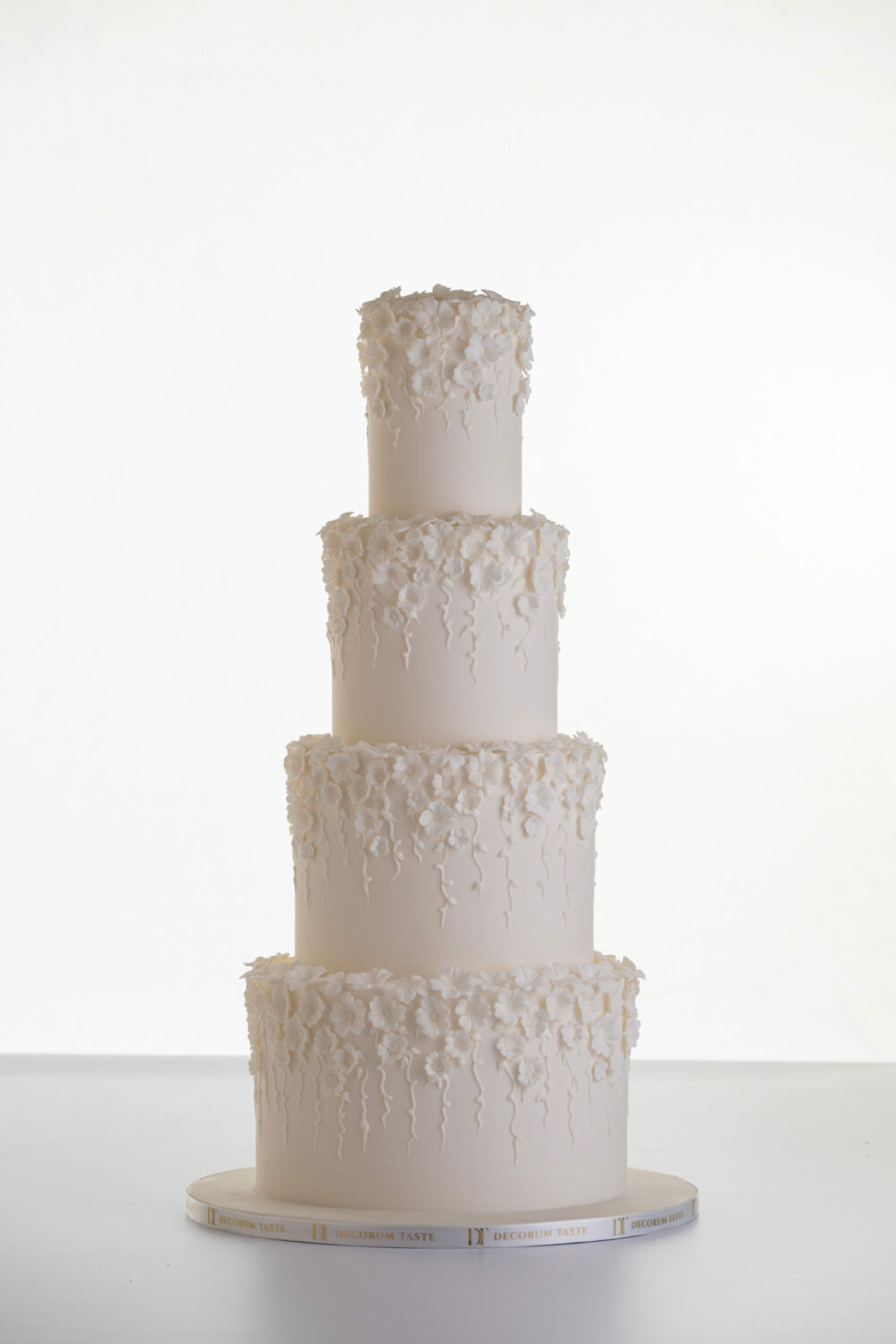 Four tier luxury contemporary, customisable, wedding cake, Fountain of Blossom, by Decorum Taste with cascades of decorative floral embellishments in ivory.