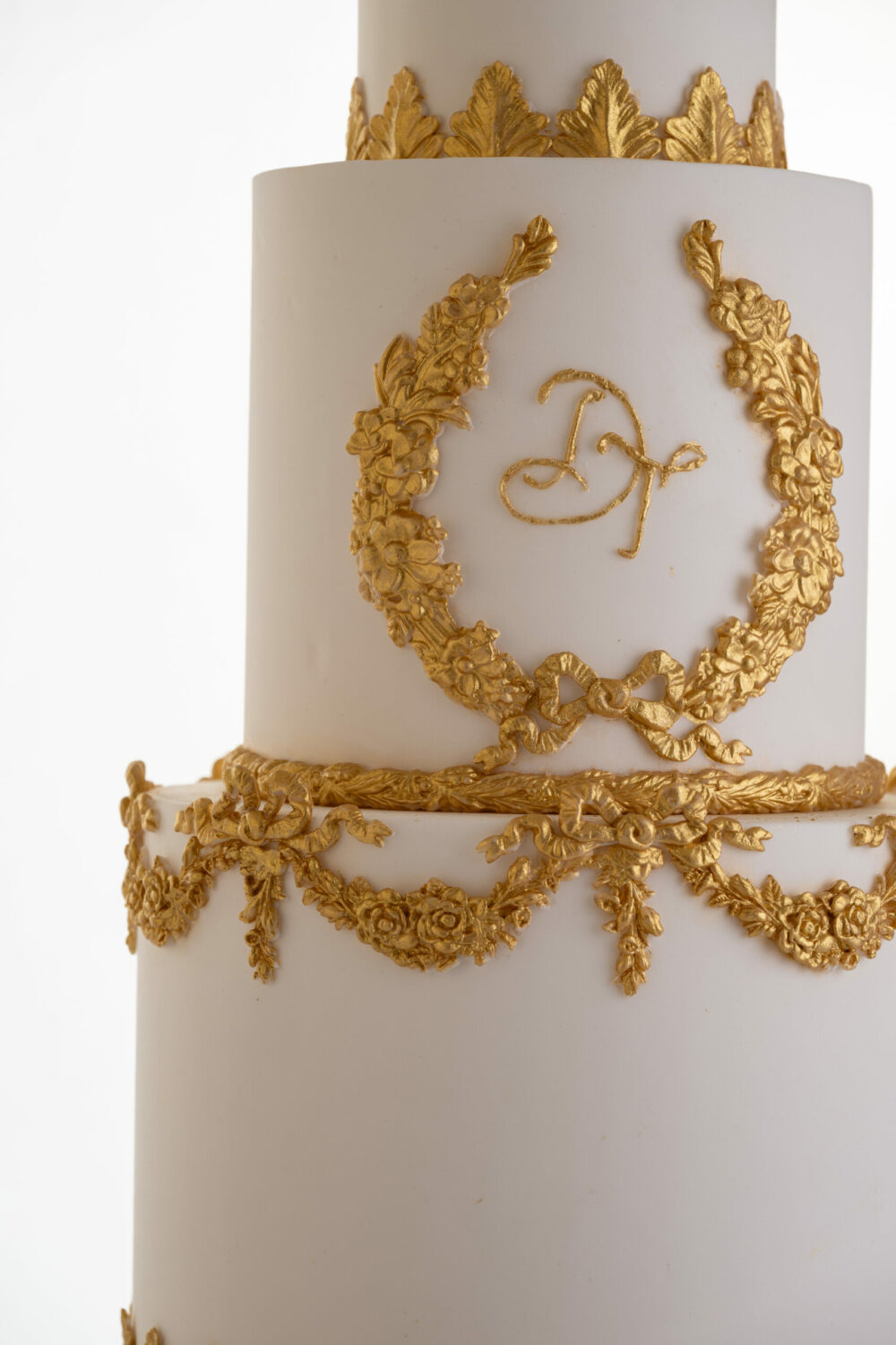 Gold monogram on luxury wedding cake, Lilibet, with gold decorative swags and bows, by Decorum Taste.