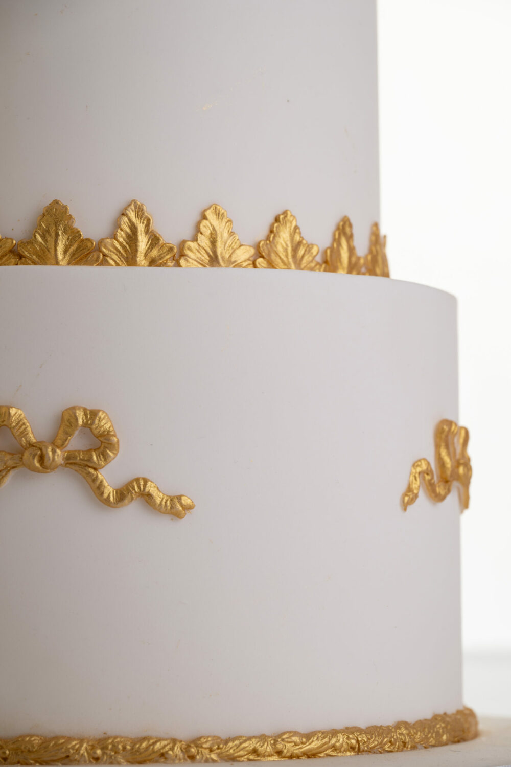 Detail of luxury customisable wedding cake with gold decorative bows by Decorum Taste.