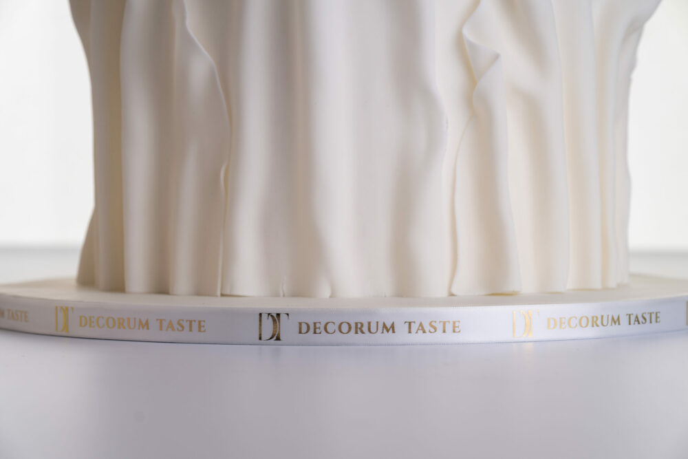 Bottom tier of luxury contemporary, customisable, wedding cake, Modern Ruffles by Decorum Taste, with textured folds and branded decorative ribbon covering the side of the cake board.