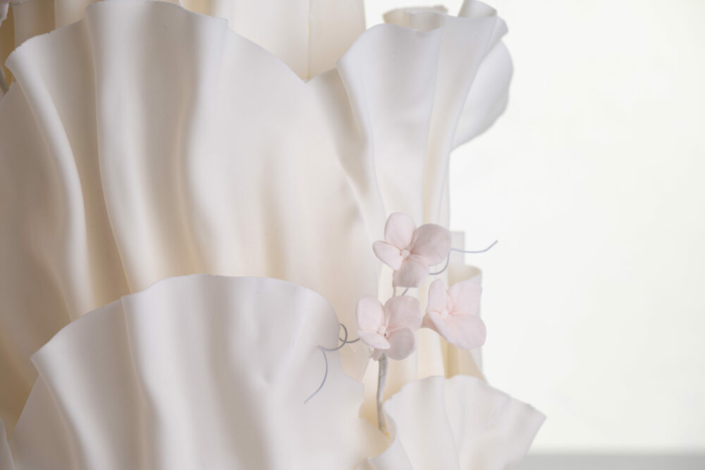 Detail of luxury contemporary, customisable, wedding cake, Modern Ruffles by Decorum Taste, with textured decorative folds and hand-crafted sugar flower stems.