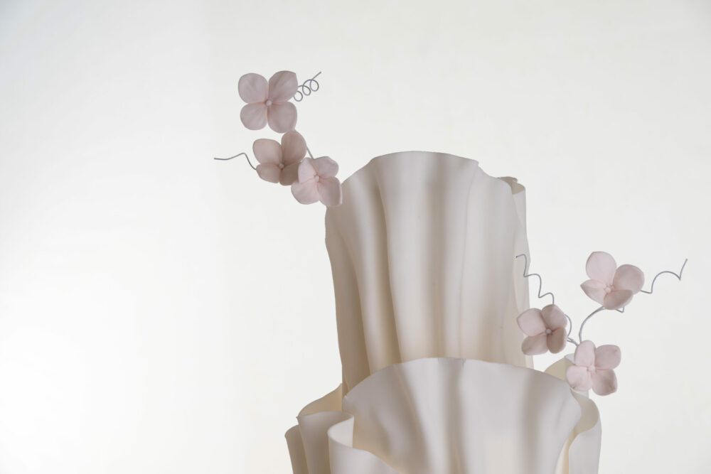 Top tier of luxury contemporary, customisable, wedding cake, Modern Ruffles by Decorum Taste, showing the textured folds of the decoration and hand-crafted sugar flower stems.