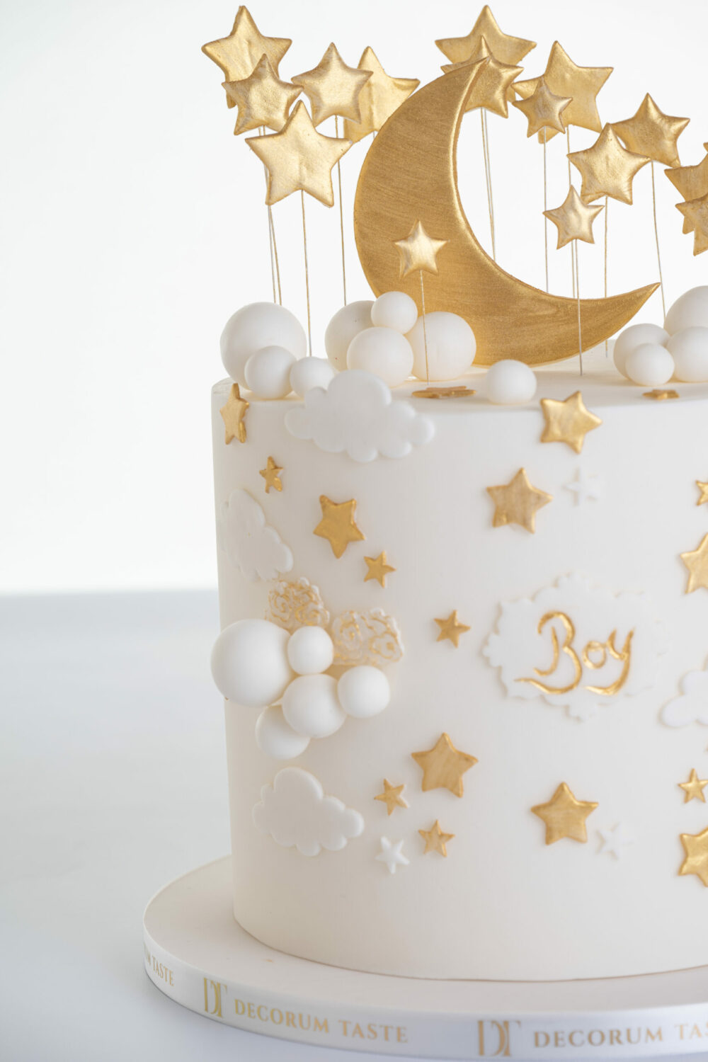 Detail of luxury contemporary, customisable, celebration cake, Moon Baby by Decorum Taste, in ivory with large golden moon, stars and clouds.