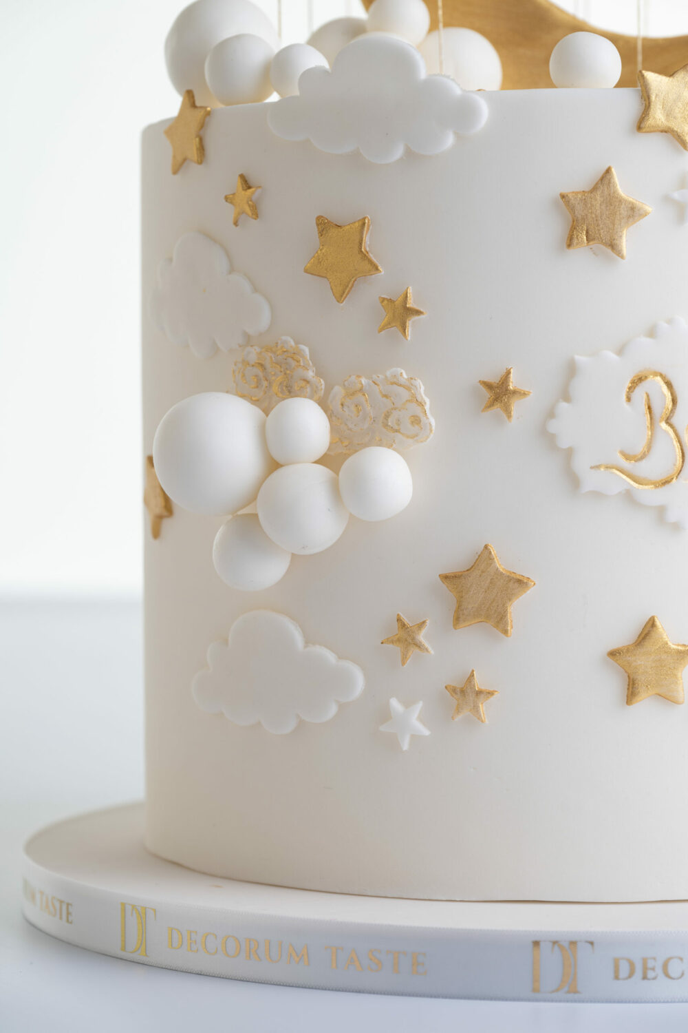 Detail of luxury contemporary, customisable, celebration cake, Moon Baby by Decorum Taste, in ivory with large golden moon, stars and clouds.