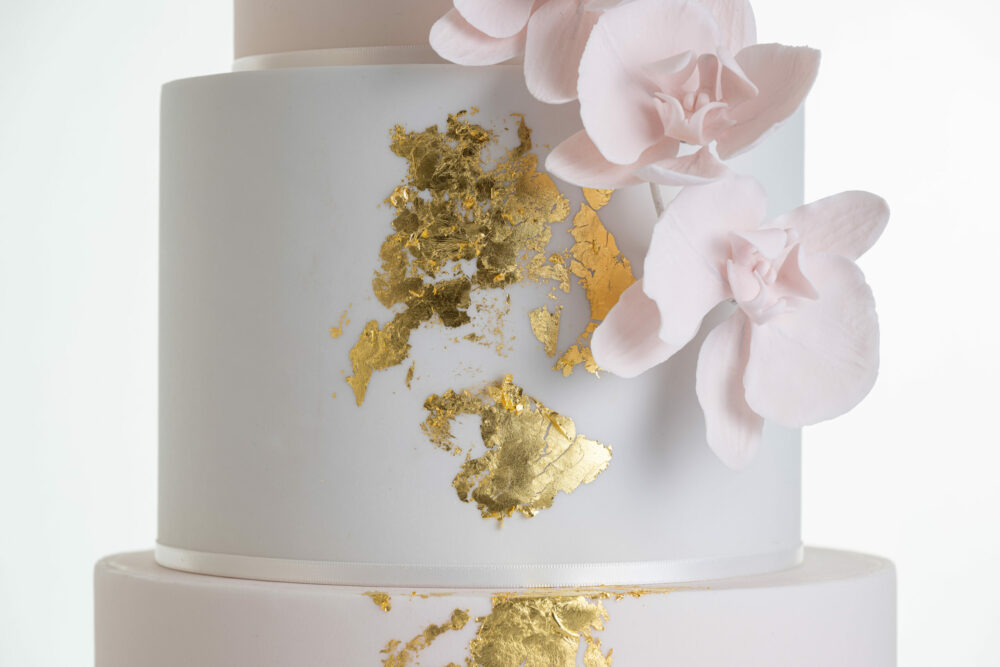 Detail of luxury contemporary, customisable, wedding cake, Orchid Heaven by Decorum Taste, with brushes of edible gold leaf and bunches hand-crafted sugar orchids.