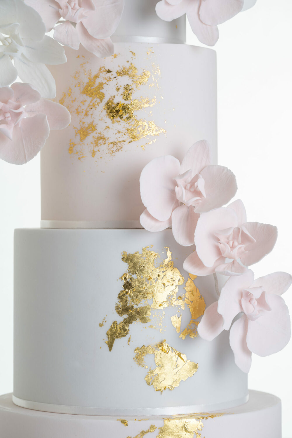 Detail of luxury contemporary, customisable, wedding cake, Orchid Heaven by Decorum Taste, with alternate tiers in blush pink and ivory, brushes of edible gold leaf and cascades of hand-crafted sugar orchids.