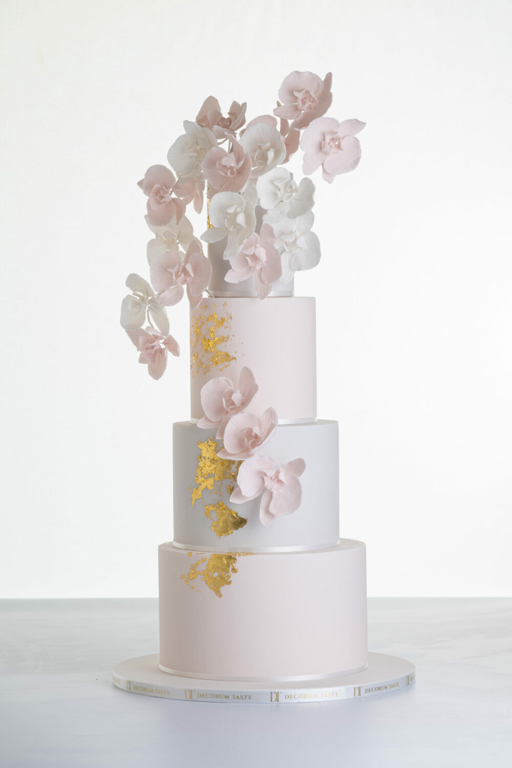 Four tier luxury contemporary, customisable, wedding cake, Orchid Heaven by Decorum Taste, with alternate tiers in blush pink and ivory, brushes of edible gold leaf and cascades of hand-crafted sugar orchids.