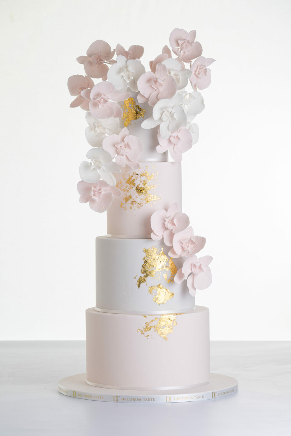 Four tier luxury contemporary, customisable, wedding cake, Orchid Heaven by Decorum Taste, with alternate tiers in blush pink and ivory, brushes of edible gold leaf and cascades of hand-crafted sugar orchids.