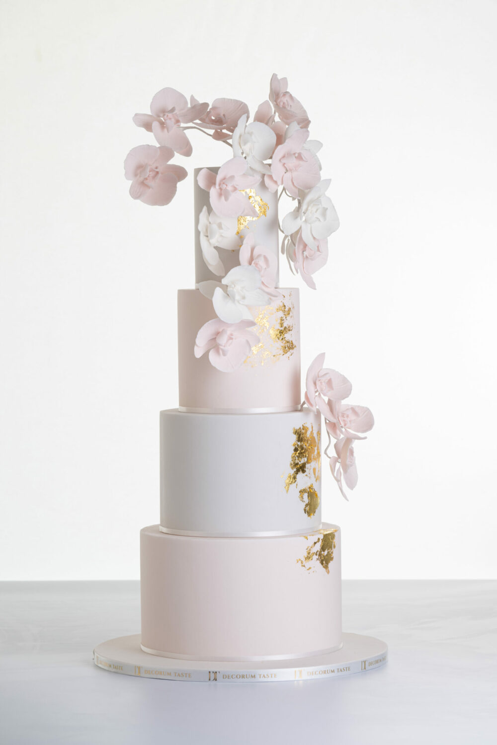 Four tier luxury contemporary, customisable, wedding cake, Orchid Heaven by Decorum Taste, with alternate tiers in blush pink and ivory, brushes of edible gold leaf and cascades of hand-crafted sugar orchids.