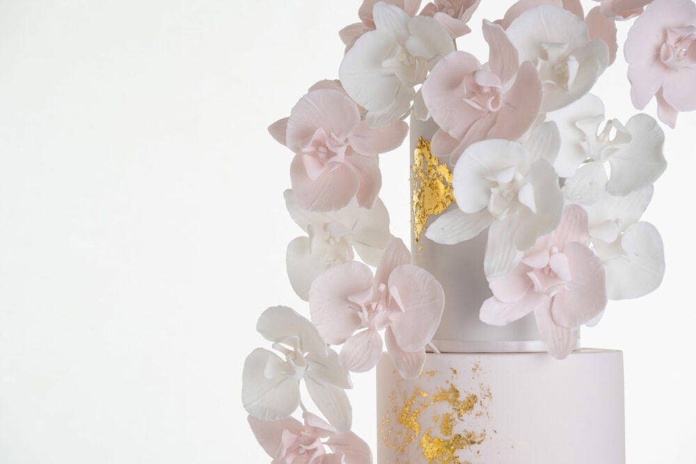 Detail of luxury contemporary, customisable, wedding cake, Orchid Heaven by Decorum Taste, with brushes of edible gold leaf and bunches hand-crafted sugar orchids.