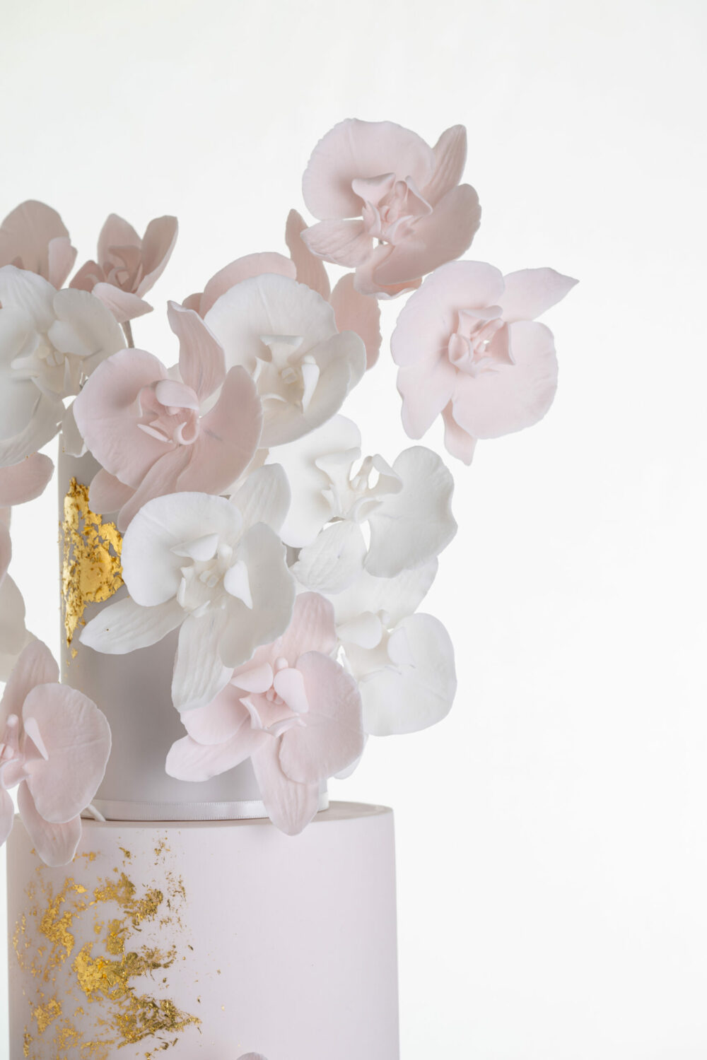 Detail of luxury contemporary, customisable, wedding cake, Orchid Heaven by Decorum Taste, with brushes of edible gold leaf and bunches hand-crafted sugar orchids.