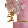 Side detail of luxury customisable contemporary wedding cake, Painted Blush by Decorum Taste, in hand-painted pink tones with gold flecks and a bouquet of hand-crafted sugar roses, hydrangea petals and trailing gold leaves.