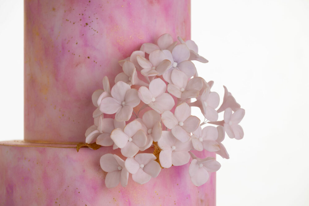 Side detail of luxury customisable contemporary wedding cake, Painted Blush by Decorum Taste, in hand-painted pink tones with bunch of hydrangea petals.