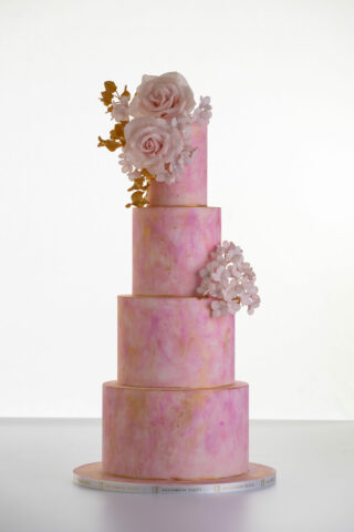 Four tier luxury customisable contemporary wedding cake, Painted Blush by Decorum Taste, in hand-painted pink tones with gold flecks, bouquet of hand-crafted sugar roses, hydrangea petals and trailing gold leaves.