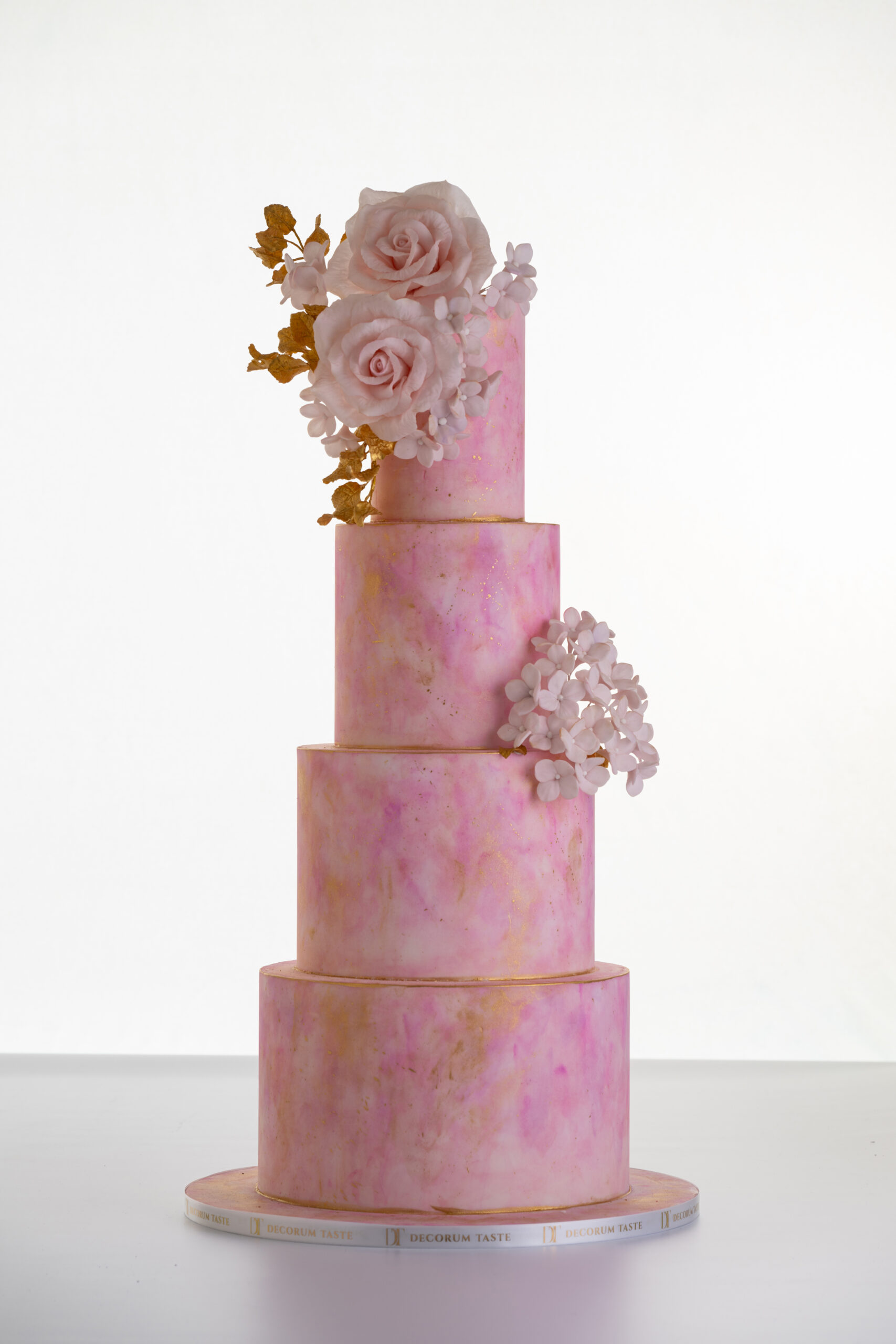 Four tier luxury customisable contemporary wedding cake, Painted Blush by Decorum Taste, in hand-painted pink tones with gold flecks, bouquet of hand-crafted sugar roses, hydrangea petals and trailing gold leaves.