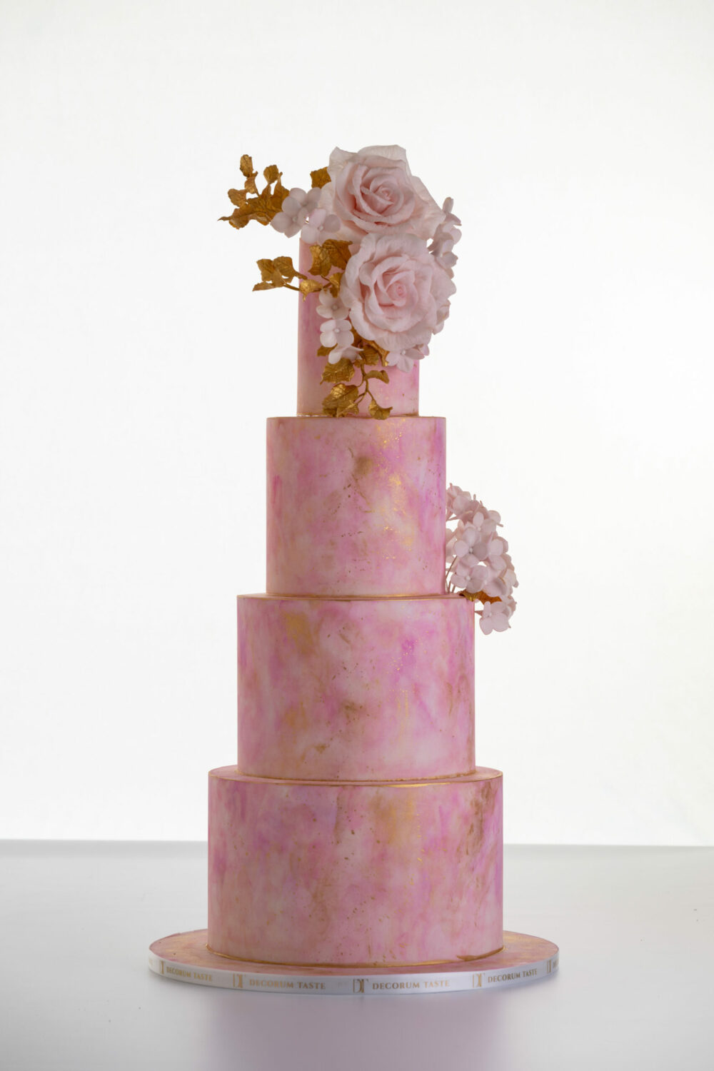 Four tier luxury customisable contemporary wedding cake, Painted Blush by Decorum Taste, in hand-painted pink tones with gold flecks, bouquet of hand-crafted sugar roses, hydrangea petals and trailing gold leaves.