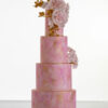 Four tier luxury customisable contemporary wedding cake, Painted Blush by Decorum Taste, in hand-painted pink tones with gold flecks, bouquet of hand-crafted sugar roses, hydrangea petals and trailing gold leaves.