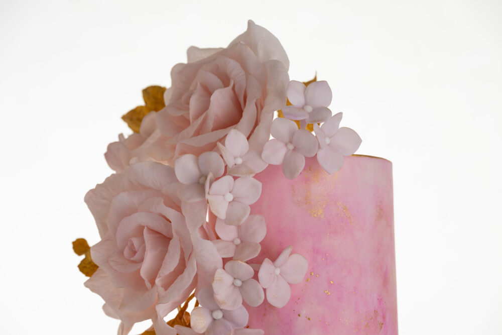 Top two tiers of luxury customisable contemporary wedding cake, Painted Blush, by Decorum Taste in pink hand-painted tones with a bouquet of large hand-crafted sugar roses, hydrangea petals and golden leaves.