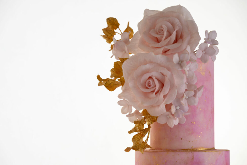 Top two tiers of luxury customisable contemporary wedding cake, Painted Blush, by Decorum Taste in pink hand-painted tones with a bouquet of large hand-crafted sugar roses, hydrangea petals and golden leaves.