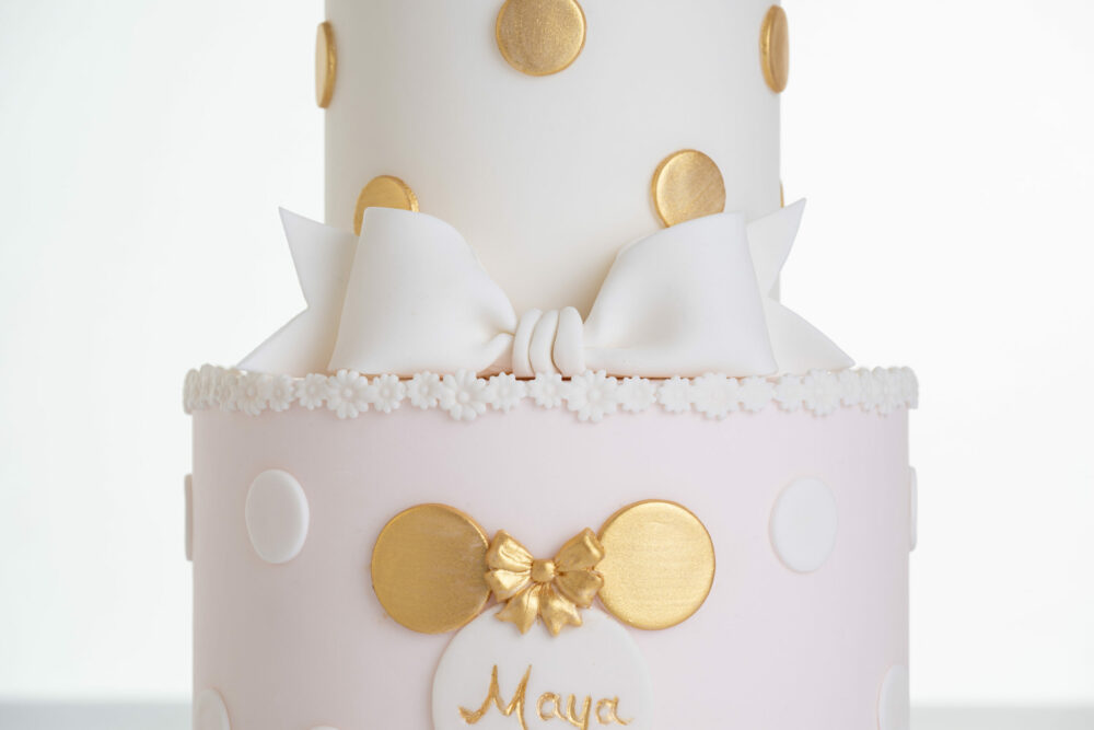 Details of luxury contemporary, customisable, celebration cake, Polka Mouse by Decorum Taste, with decorative edible gold leaf circle embellishments, a pretty floral trim and sugar paste bow.