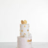 Two tier luxury contemporary, customisable, celebration cake, Polka Mouse by Decorum Taste, with decorative edible gold leaf circle embellishments, a pretty floral trim, cartoon mouse ears and sugar paste bow.