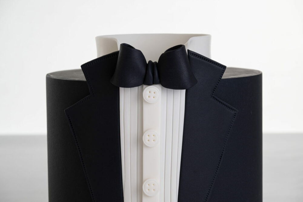 Detail of luxury contemporary, customisable, celebration cake, Tux Gent by Decorum Taste decorated in black the white of a formal shirt, tuxedo jacket and bow tie.