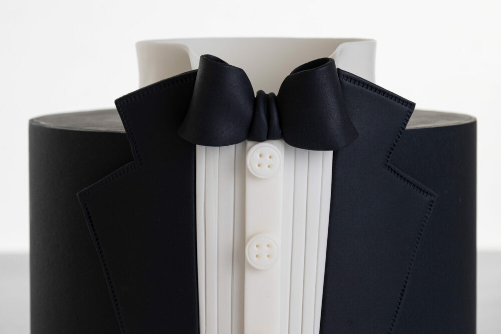 Detail of luxury contemporary, customisable, celebration cake, Tux Gent by Decorum Taste decorated in black the white of a formal shirt, tuxedo jacket and bow tie.