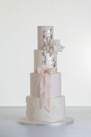 Four tier luxury contemporary, customisable, wedding cake, Vintage Beauty by Decorum Taste with large hand-crafted sugar rose in ivory, brushed edible silver leaf, decorative floral embellishments and a pink silk bow.