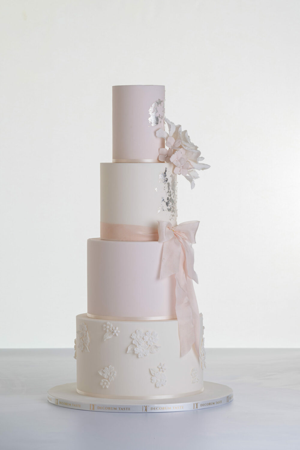 Four tier luxury contemporary, customisable, wedding cake, Vintage Beauty by Decorum Taste with large hand-crafted sugar rose in ivory, brushed edible silver leaf, decorative floral embellishments and a pink silk bow.