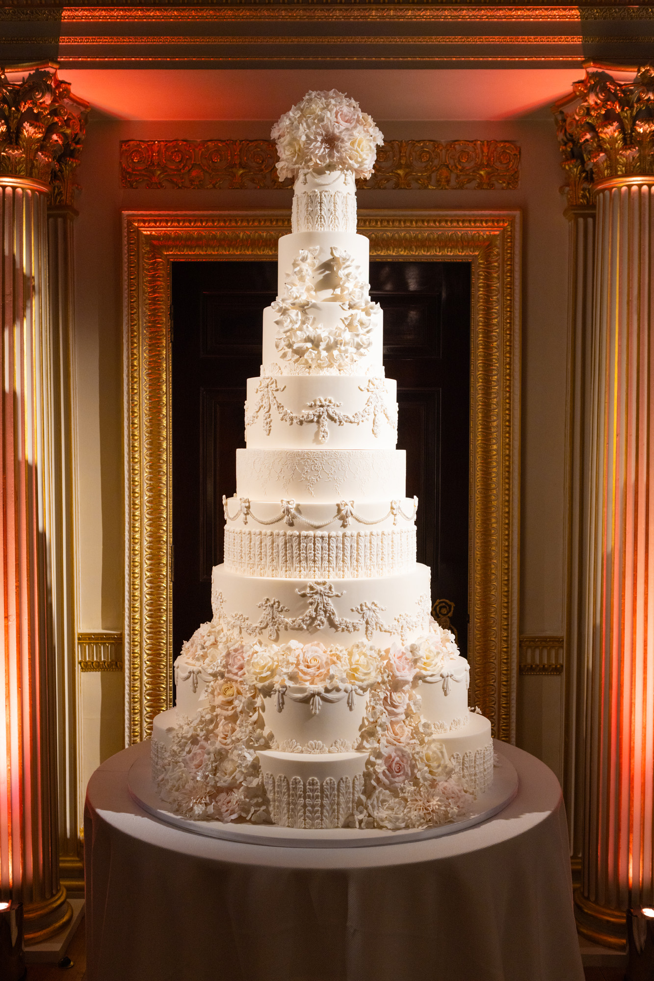 Luxury bespoke wedding cake, Princess Grace By Yevnig, an impressive 10 tier cake covered in ivory Royal icing with piped swags, bow and other decorative elements and life-like hand-crafted sugar flower cascades and bouquets